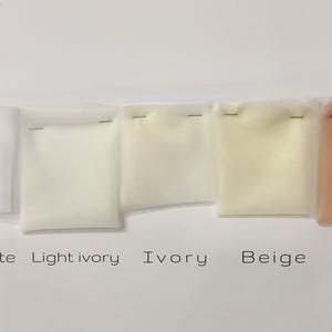 May include: A collection of fabric swatches in shades of white, ivory, beige, and pink, labeled "Pure white," "Light ivory," "Ivory," "Beige," and "Pink." Each swatch is stapled to a small square of clear plastic.
