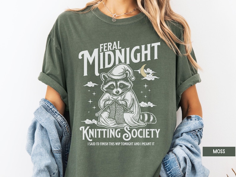 Puede incluir: Camiseta verde musgo con un dise&ntilde;o de un mapache tejiendo, con gorro de dormir, y las palabras "Feral Midnight Knitting Society". El texto "I said I'd finish this WIP tonight and I meant it" est&aacute; debajo.