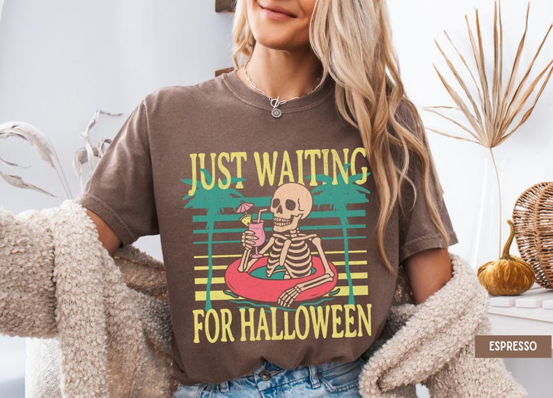 Peut inclure: T-shirt marron avec l'inscription &laquo; JUST WAITING FOR HALLOWEEN &raquo;. Le motif repr&eacute;sente un squelette dans une bou&eacute;e avec un cocktail, sur fond de palmiers et de coucher de soleil.