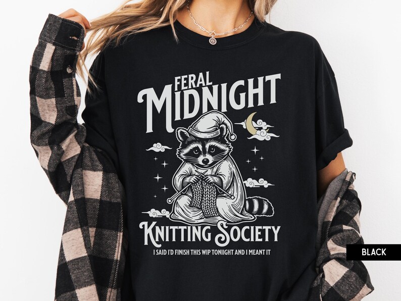 Puede incluir: Camiseta negra con un mapache con gorro de dormir, tejiendo. El texto dice "FERAL MIDNIGHT KNITTING SOCIETY" con la frase "I SAID I'D FINISH THIS WIP TONIGHT AND I MEANT IT".
