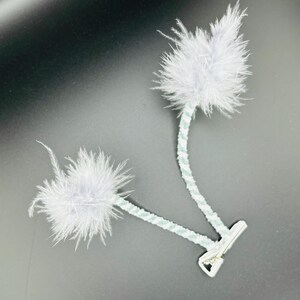 May include: Two white feather pom-poms attached to a blue and white striped cord with a silver clip.