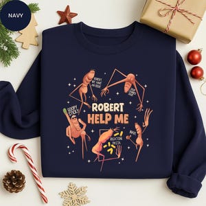 May include: Navy blue sweatshirt with a graphic featuring the text "ROBERT HELP ME" surrounded by cartoon figures and text bubbles. The text bubbles say "GOOPY STICKY", "ROBERT WE HAVE AN ISSUE", "SOUP CANNED SOUP", "RIGATONI PASTA", and "NAH".