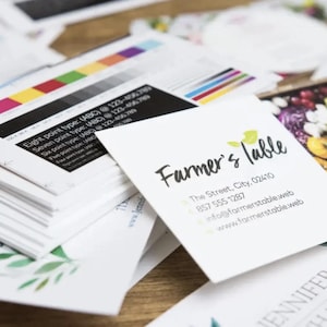 May include: A stack of white business cards with a green leafy design. The top card has the text "Farmer's Table" in black script font with the business's address and phone number below.
