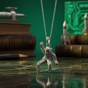 Pu&ograve; includere: Collana con pendente in argento raffigurante una figura umana stilizzata con un motivo geometrico. Il pendente &egrave; appeso a una delicata catena. Lo sfondo include libri, una penna e modelli di razzi in miniatura.