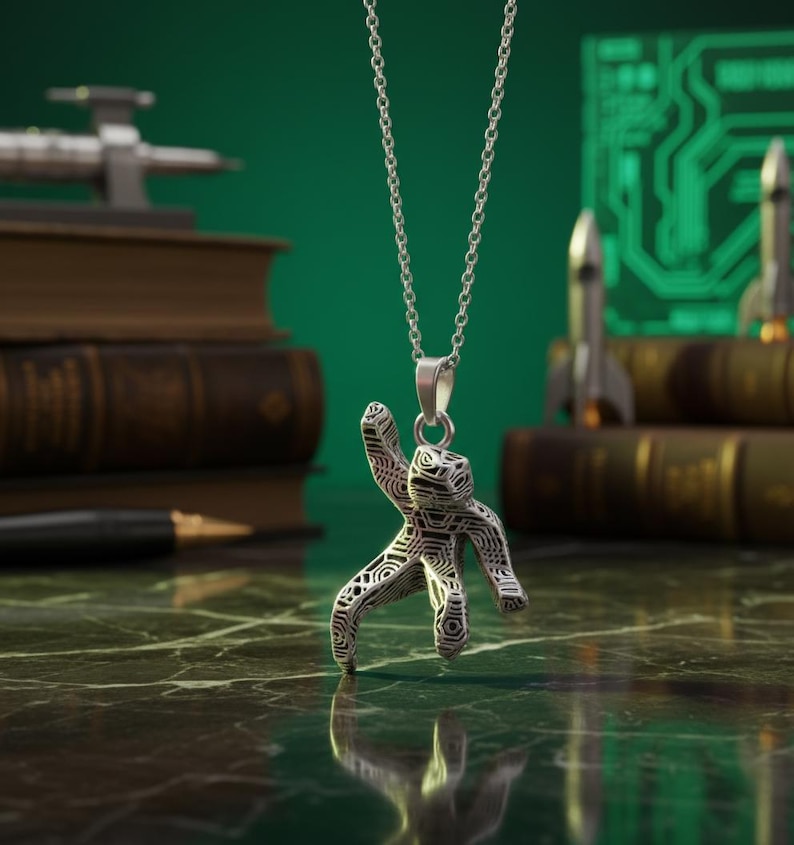 Pu&ograve; includere: Collana con pendente in argento raffigurante una figura umana stilizzata con un motivo geometrico. Il pendente &egrave; appeso a una delicata catena. Lo sfondo include libri, una penna e modelli di razzi in miniatura.