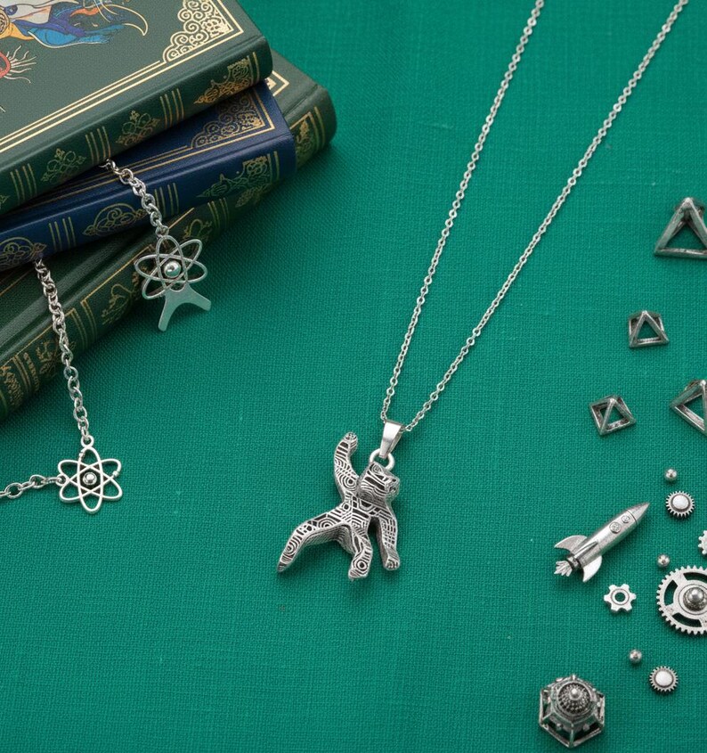 Pu&ograve; includere: Una collana argentata con un ciondolo a forma di astronauta stilizzato, esposta su una superficie verde. Altri ciondoli a tema scientifico, tra cui un atomo, un razzo e ingranaggi, sono sparsi. Libri con copertine verdi e blu sono sullo sfondo.