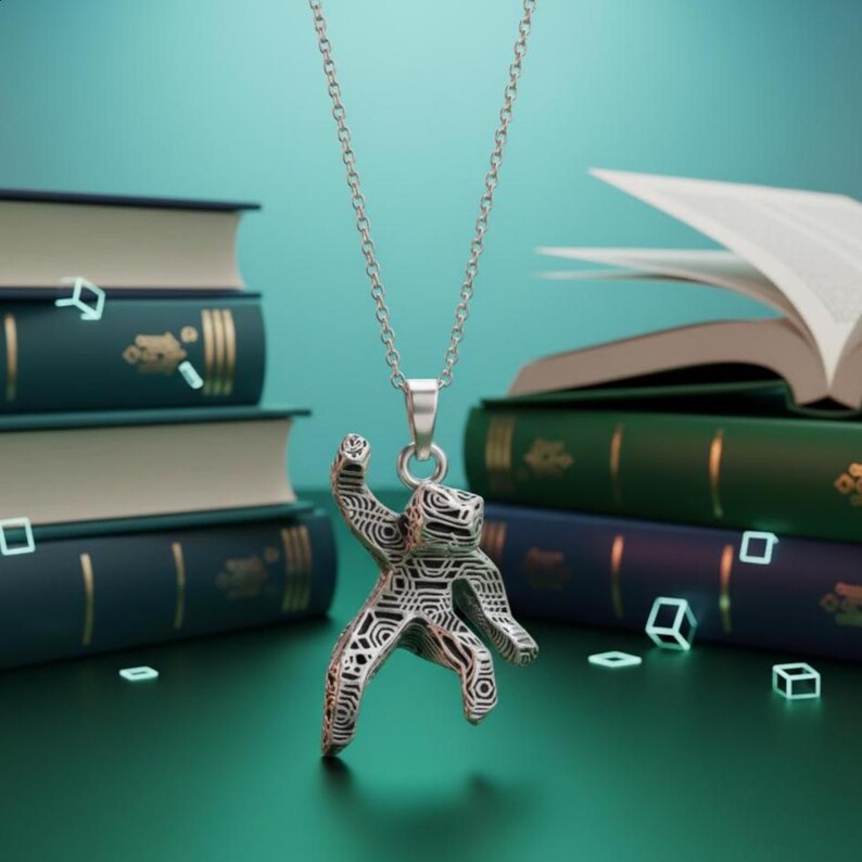 Pu&ograve; includere: Una collana con pendente argentato raffigurante una figura stilizzata con un motivo geometrico. Il pendente &egrave; appeso a una catena sottile. Lo sfondo presenta pile di libri in tonalit&agrave; verdi e blu.