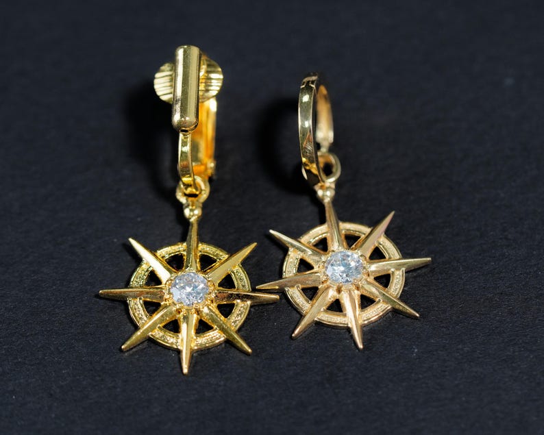 K&ouml;nnte beinhalten: Ein Paar goldfarbene Ohrclips mit einem Sternendesign und einem klaren Strassstein in der Mitte.