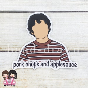May include: A sticker featuring a cartoon illustration of a person with brown hair wearing a striped red and white shirt. The text "pork chops and applesauce" is below the illustration.