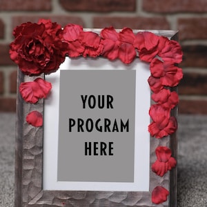 Puede incluir: Un marco de fotos de madera con interior gris y el texto "YOUR PROGRAM HERE". El marco está decorado con flores y pétalos de tela roja, creando un borde floral alrededor del marco.