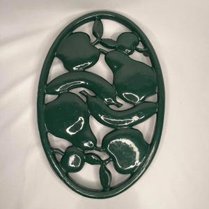 May include: Green cast iron oval hot pad with a design of pears and apples.