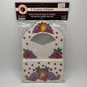 May include: Two hanging notepads in a clear plastic package. The notepads are decorated with a fruit design of grapes, apples, and strawberries. Each notepad measures 3 1/8 x 5 5/8 inches.