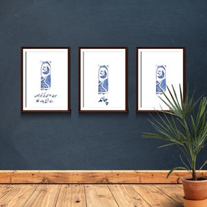 May include: Three framed prints with a blue and white illustration of a sleeping cat with a crescent moon above it. The left print has the text "میں خوابوں کی راہوں سے چلتا ہوں" in Urdu. The middle print has the text "چاند" in Urdu. The right print has no text.