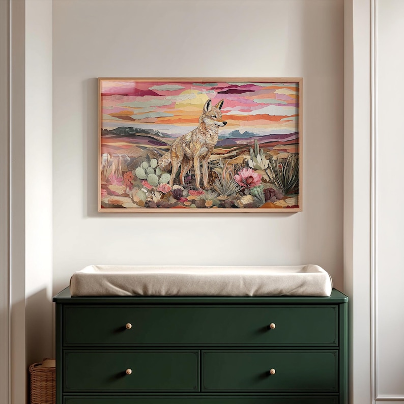May include: A framed art print featuring a coyote in a desert landscape with cacti and blooming flowers. The artwork has a warm color palette of pinks, oranges, and purples, with a wooden frame. The print is displayed above a dark green dresser.