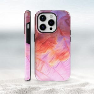 Peut inclure: Coque de téléphone ornée d'un motif de plumes aux couleurs vives, avec des nuances de rose, d'orange et de violet. L'image présente la coque de face et de côté, mettant en valeur l'impression enveloppante et les détails de l'appareil photo et des boutons du téléphone.