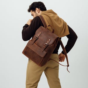 May include: A brown leather backpack with a flap closure and two buckle straps. The backpack has a front pocket and adjustable shoulder straps. The bag is made of a distressed leather material.