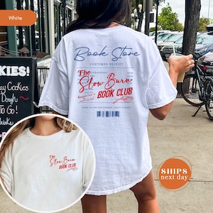 A white t-shirt with text and logos printed on it, featuring a woman's back and a bicycle in the background.