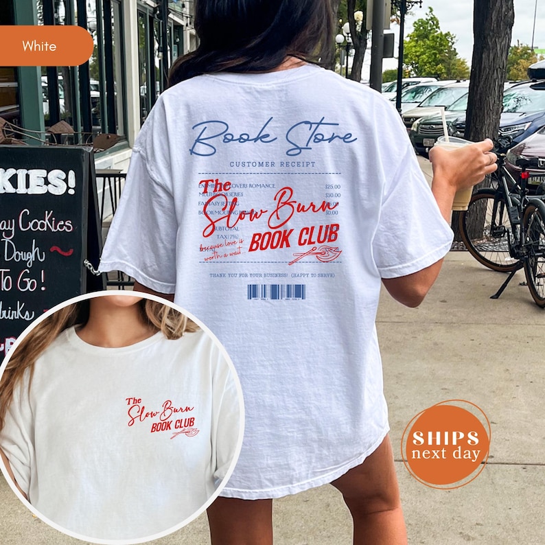 A white t-shirt with text and logos printed on it, featuring a woman's back and a bicycle in the background.