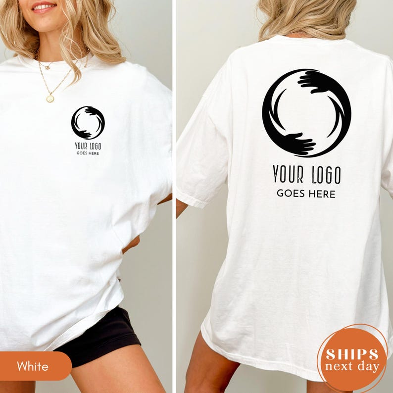 May include: A white t-shirt featuring a black circular graphic of two hands reaching toward each other on the left chest and a larger version of the same graphic on the back. The text "YOUR LOGO GOES HERE" is printed below the graphic in both locations.