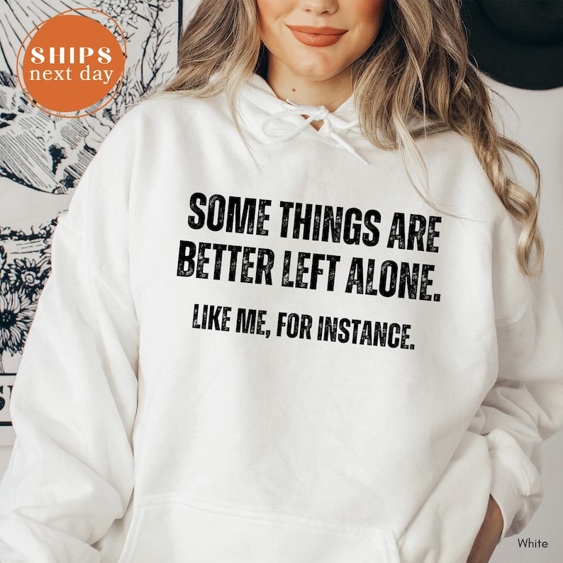 A woman wearing a white hoodie with the text "Some things are better left alone. Like me, for instance." printed on it.