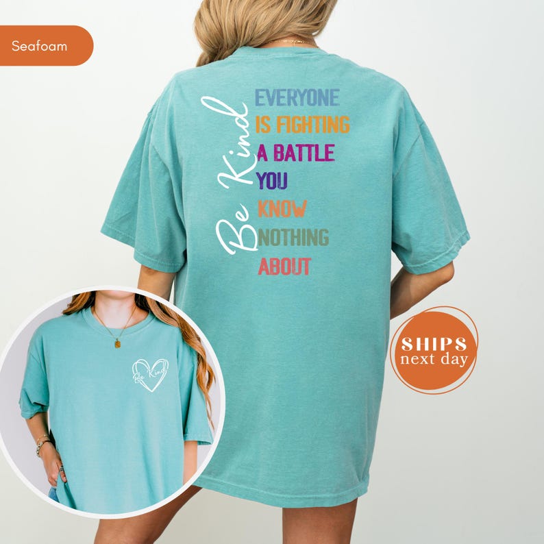 May include: Seafoam green t-shirt with the words "Be Kind" in a script font. The back of the shirt has the message "Everyone is fighting a battle you know nothing about" in various colors. A small heart design is on the front.