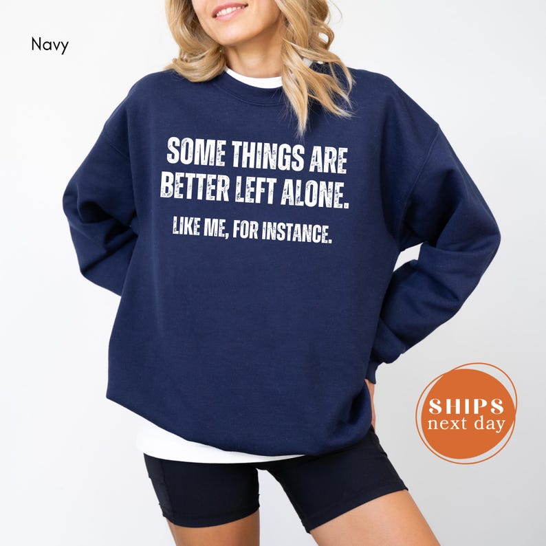A woman wearing a navy blue sweatshirt with the text "Some things are better left alone. Like me, for instance."