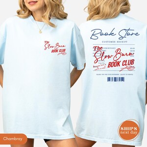 a woman wearing a white t-shirt with text and logos related to a book store and a book club.