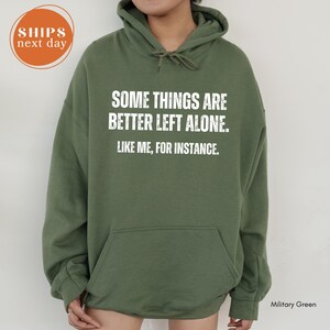 A person wearing a green hoodie with white text that reads "Some things are better left alone. Like me, for instance."