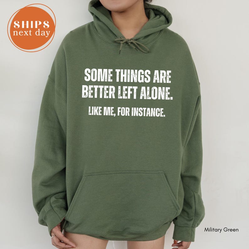 A person wearing a green hoodie with white text that reads "Some things are better left alone. Like me, for instance."