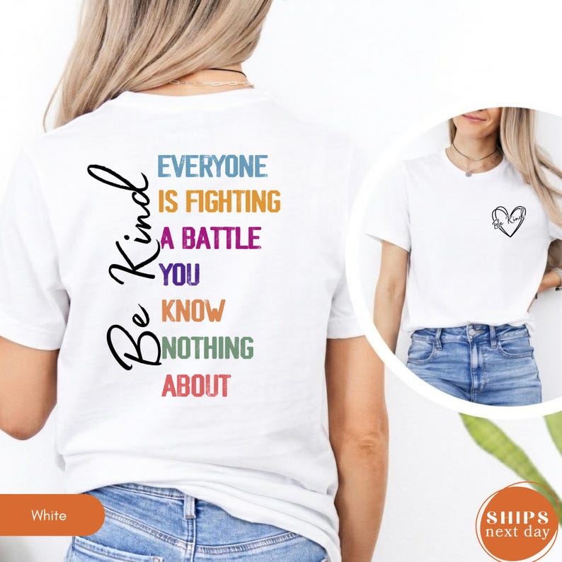 May include: White t-shirt with the words "Be Kind" in black script on the back. The shirt also features the text "EVERYONE IS FIGHTING A BATTLE YOU KNOW NOTHING ABOUT" in various colors. A small heart design is on the front.