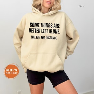 A person wearing a beige hoodie with the text "Some things are better left alone. Like me, for instance." printed on it.