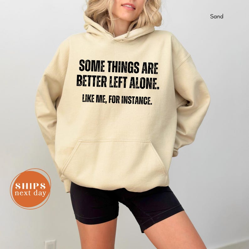 A person wearing a beige hoodie with the text "Some things are better left alone. Like me, for instance." printed on it.