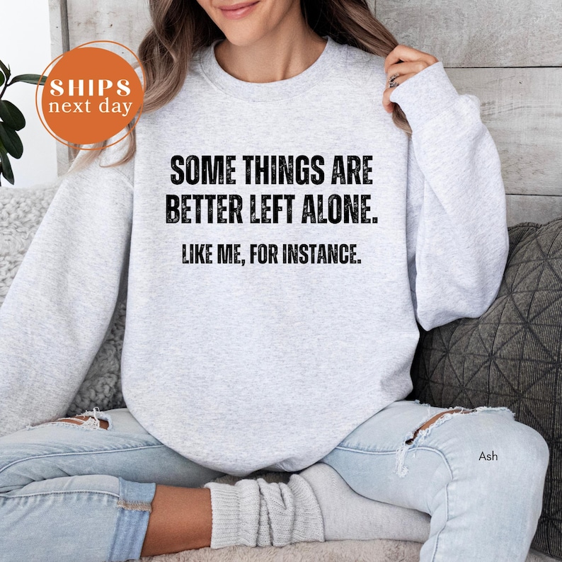 A woman wearing a gray sweatshirt with the text "Some things are better left alone. Like me, for instance." printed on it.