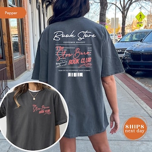 a person wearing a gray t-shirt with text and logos related to a book store and a book club.