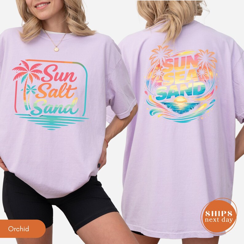 May include: A light purple short-sleeve t-shirt featuring a graphic on the front and back. The front graphic shows a palm tree and the text Sun Salt Sand. The back graphic displays palm trees, a sunset, and the text SUN SEA SAND.