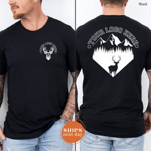 May include: Black t-shirt with a white deer head logo on the front and a mountain and deer graphic on the back. The text "YOUR LOGO HERE" is printed above the mountain graphic. The shirt is made of a soft material.
