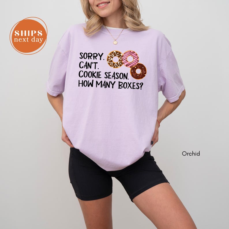 A woman wearing a purple t-shirt with a humorous text printed on it, standing against a white background.