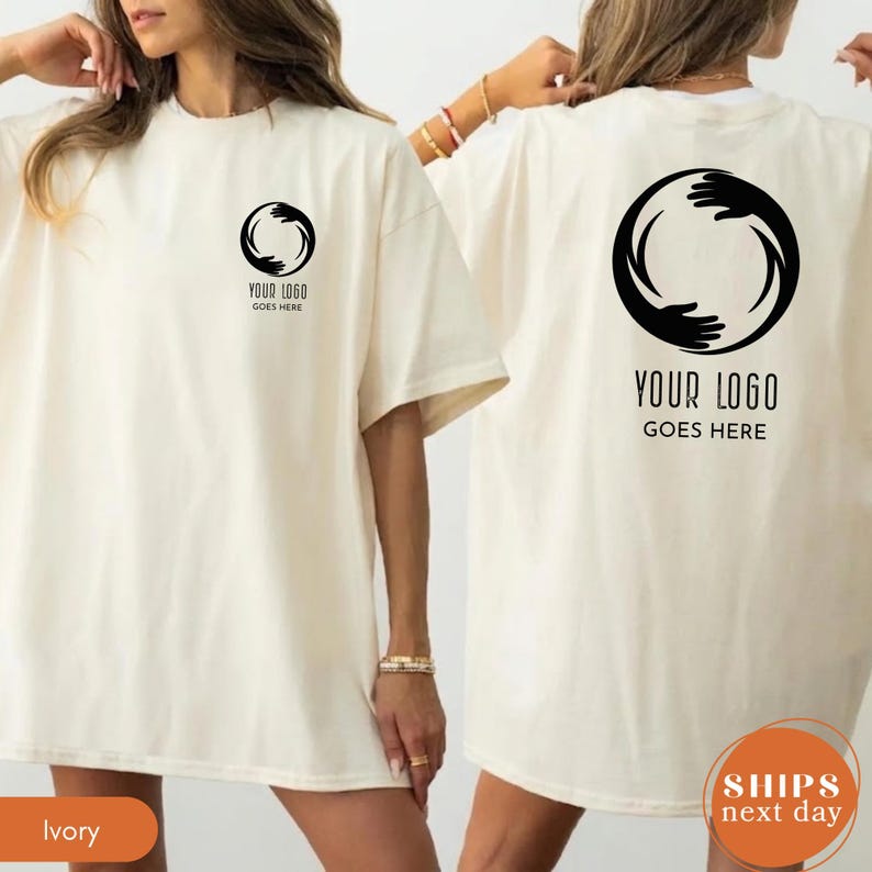 May include: An ivory t-shirt featuring a black circular graphic of hands on the left chest and a larger version of the same graphic on the back. The text "YOUR LOGO GOES HERE" is printed in black below both the small and large circular hand designs.
