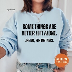 A person wearing a light blue sweatshirt with the text "SOME THINGS ARE BETTER LEFT ALONE. LIKE ME, FOR INSTANCE." printed on it.