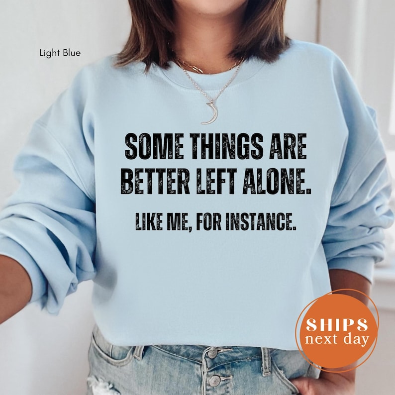 A person wearing a light blue sweatshirt with the text "SOME THINGS ARE BETTER LEFT ALONE. LIKE ME, FOR INSTANCE." printed on it.