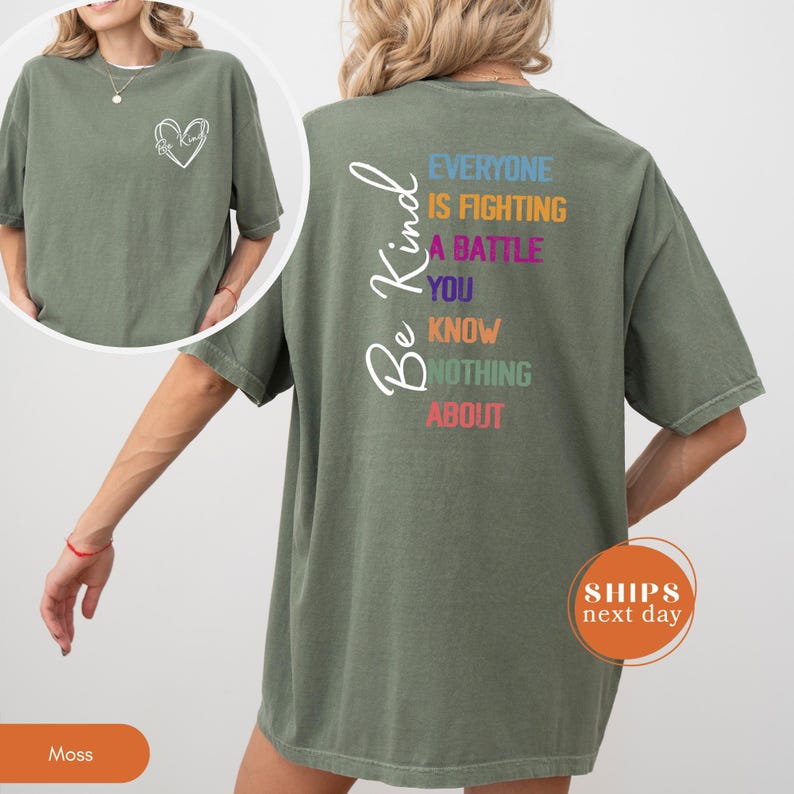 May include: Moss green t-shirt with a white heart outline on the front and the words "Be Kind" on the back. The back of the shirt also has the text "Everyone is fighting a battle you know nothing about" in various colors.