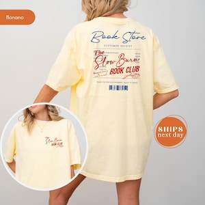 A woman wearing a yellow t-shirt with text and logos related to a book store and a slow-burning book club.