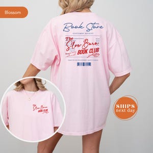 A woman wearing a pink t-shirt with text and logos related to a book store and a book club.