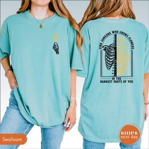 A woman wearing a teal t-shirt with a graphic design on the back.