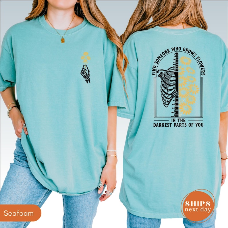 A woman wearing a teal t-shirt with a graphic design on the back.