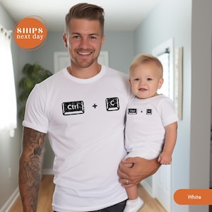 May include: White t-shirts with black keyboard key graphics. One shirt displays "Ctrl + C", the other "Ctrl + V". The shirts are worn by an adult and a baby. The image also includes the text "SHIPS next day" and the word "White".