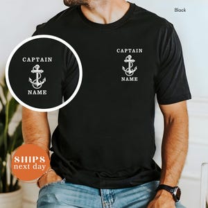 May include: Black t-shirt with a white anchor graphic and the text "CAPTAIN" above and "NAME" below. The shirt has a crew neck and short sleeves. The word "Black" is in the upper right corner.