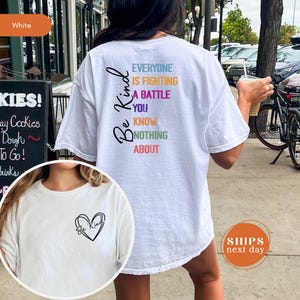 May include: White t-shirt with the words "Be Kind" and a heart design on the front. The back of the shirt has the phrase "Everyone is fighting a battle you know nothing about" in colorful text.