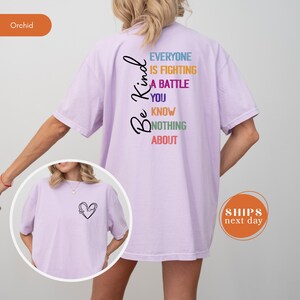 May include: A light purple t-shirt with the words "Be Kind" and "Everyone is fighting a battle you know nothing about" in black, blue, purple, green, and red. A small image of a heart with the words "Be Kind" is on the front.