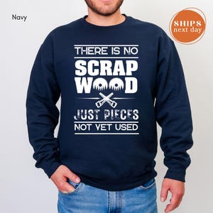 May include: Navy blue sweatshirt with white text: "THERE IS NO SCRAP WOOD JUST PIECES NOT YET USED." The design includes a saw blade and crossed saws. A round orange sticker says "SHIPS next day".